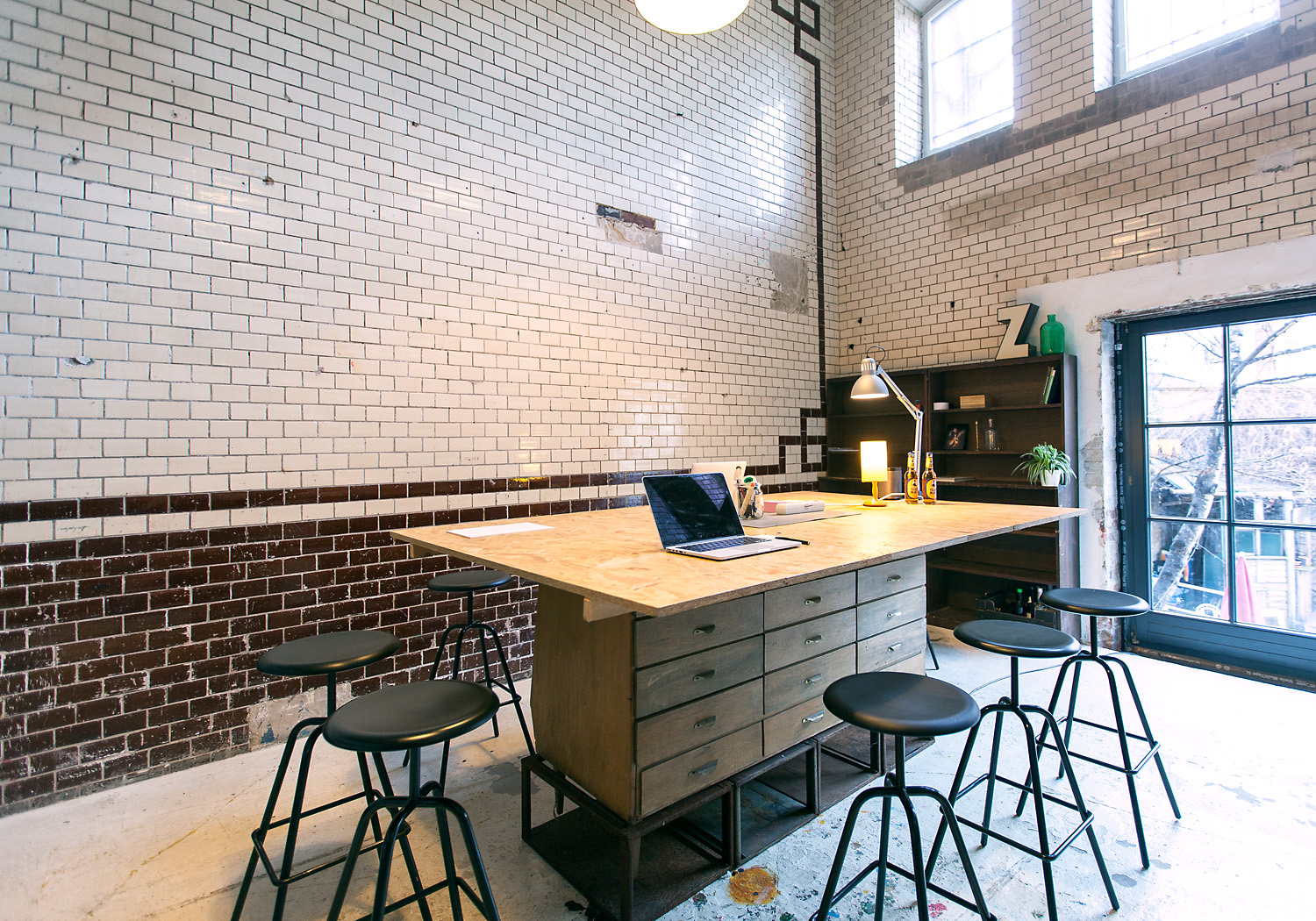 Upper florr of the coworking space showing a high ceiling room with a big shared desk and bar stools